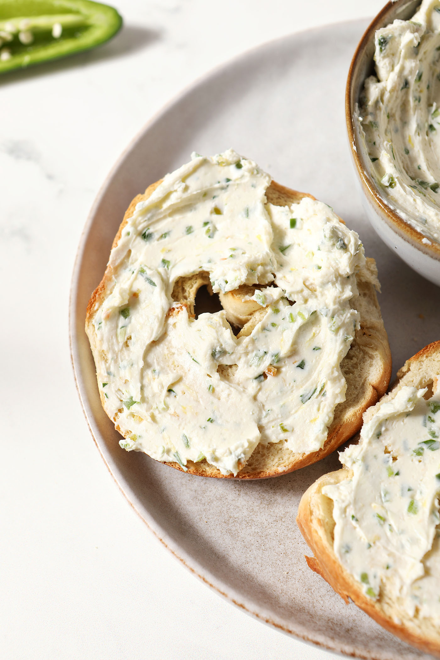 A halved bagel slathered in Jalapeno Cream Cheese on a grey plate on a marble surface