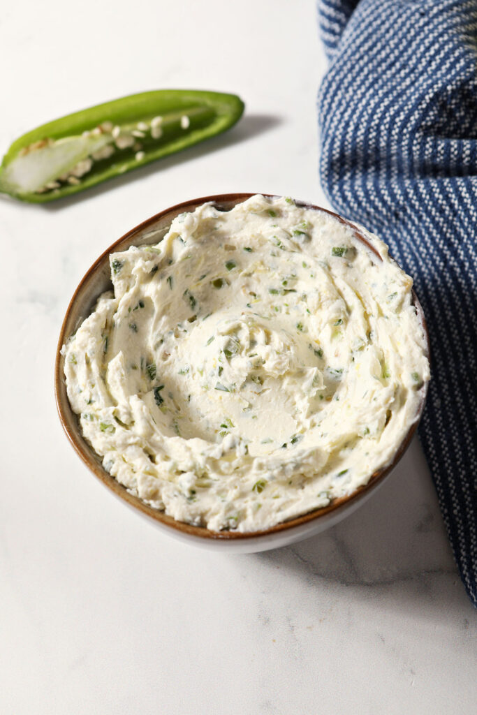 A bowl of jalapeño cream cheese on a marble surface next to a blue linen