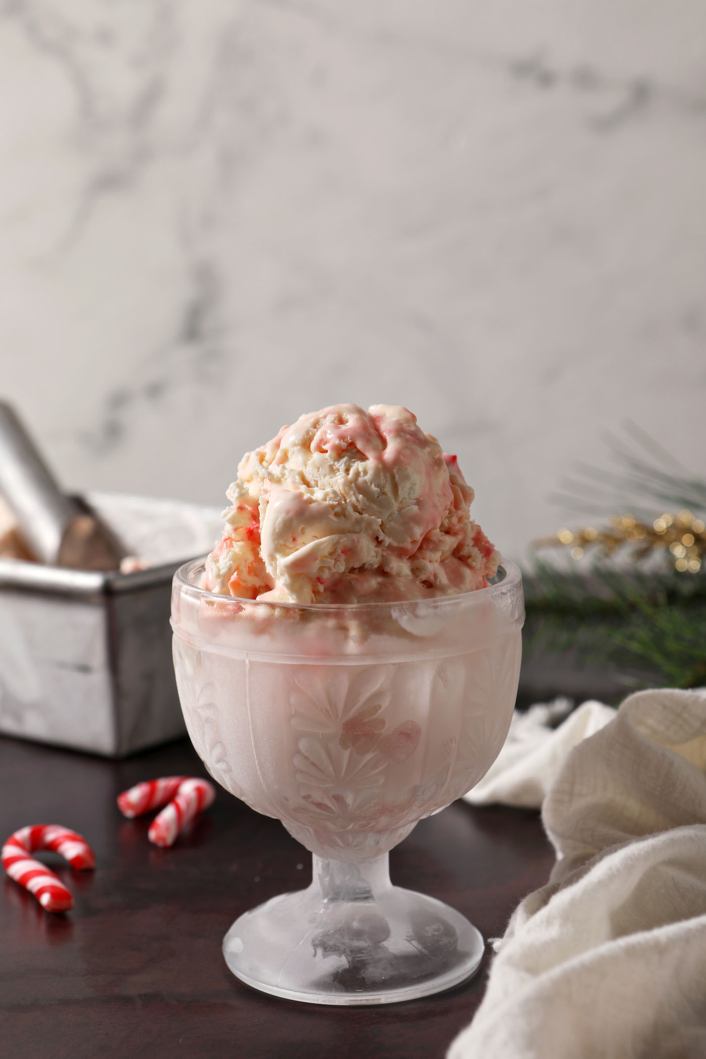 Scoops of No Churn Peppermint Ice Cream in a chilled glass on a dark red surface in front of a loaf pan
