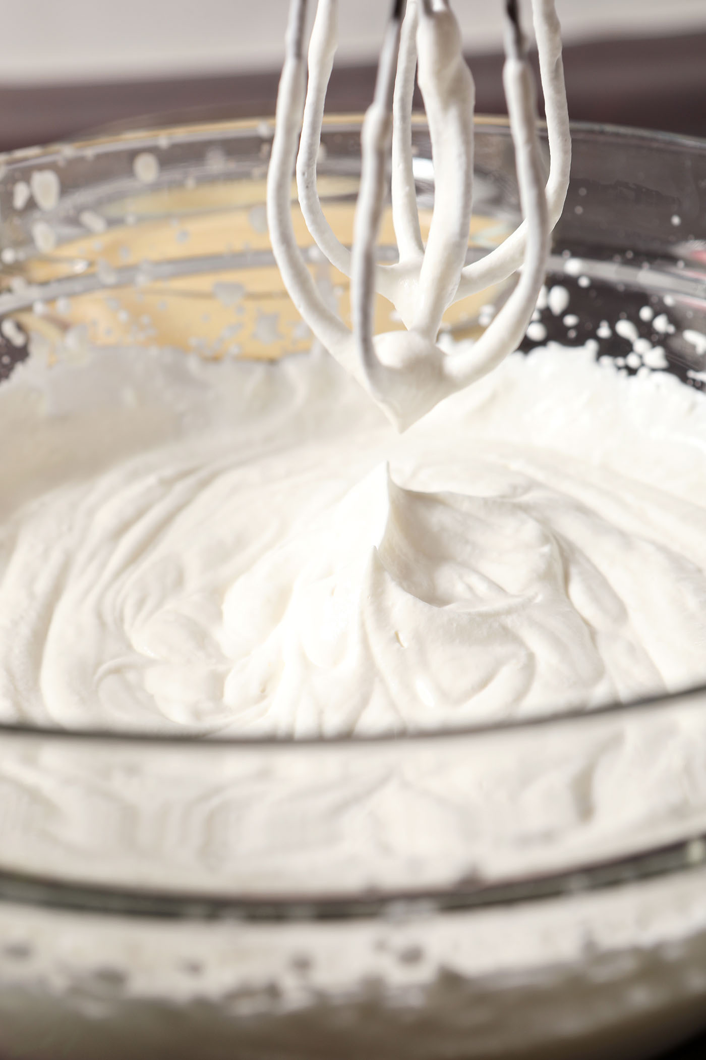 Mixer beaters lift out of a bowl of whipped cream, showing soft peaks