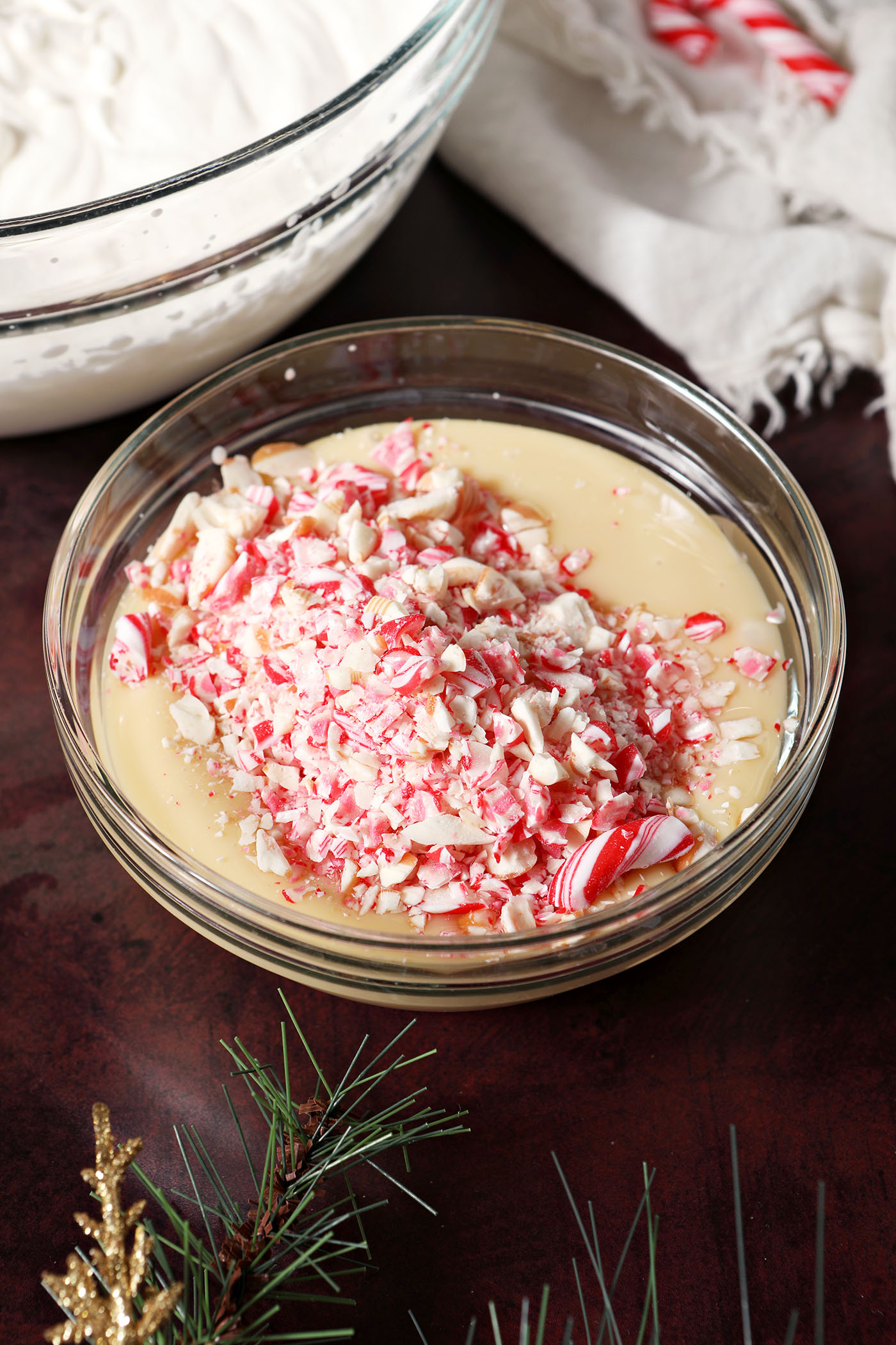 Crushed candy canes, peppermint extract and sweetened condensed milk in a bowl on a dark red surface, before mixing