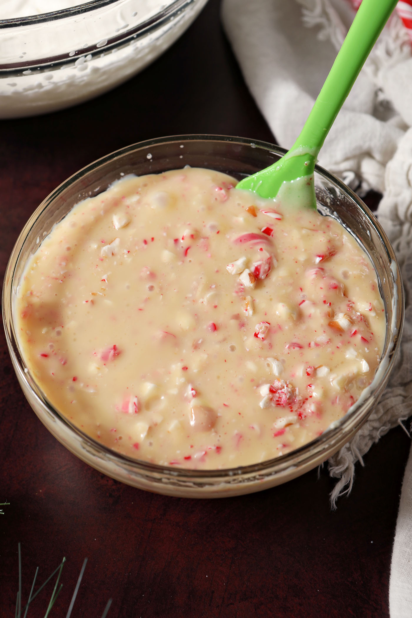 Crushed candy canes, peppermint extract and sweetened condensed milk in a bowl on a dark red surface, after mixing