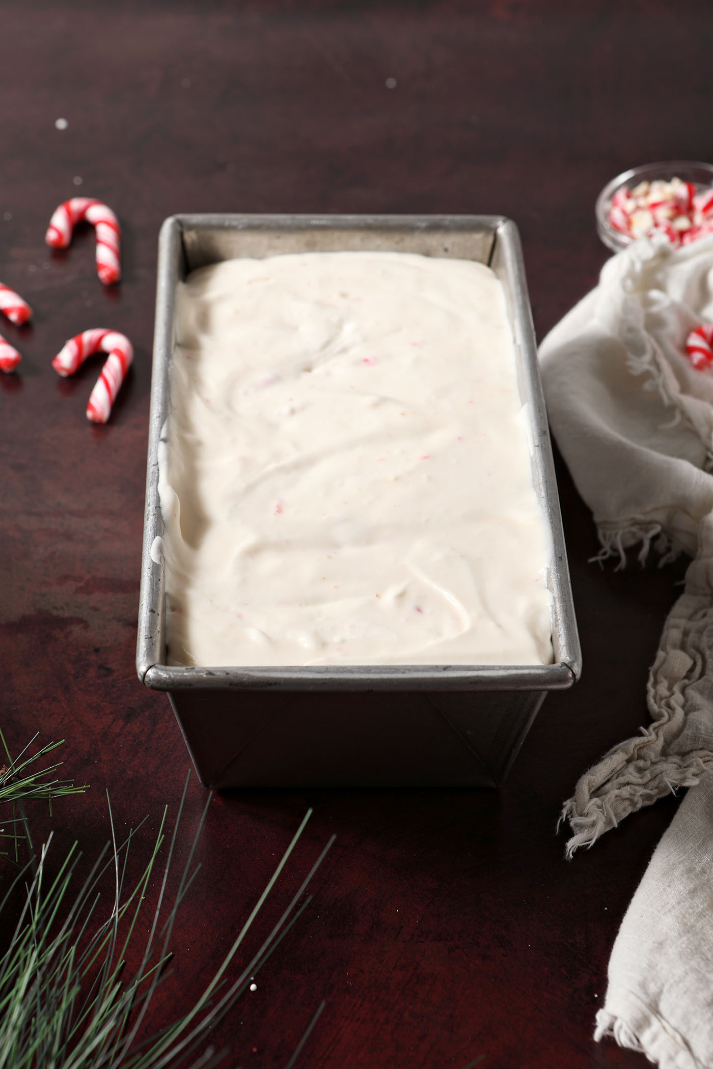 No Churn Peppermint Ice Cream in a loaf pan on a dark red surface, before freezing