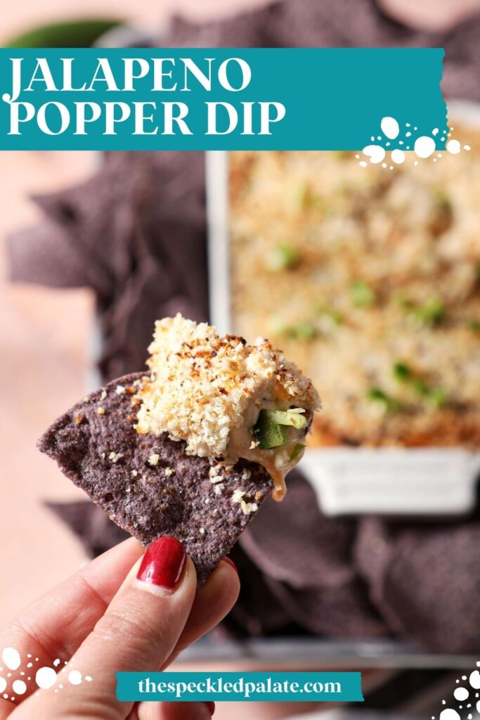 A hand holds a blue corn tortilla chip after dipping into baked jalapeño popper dip with the text jalapeno popper dip