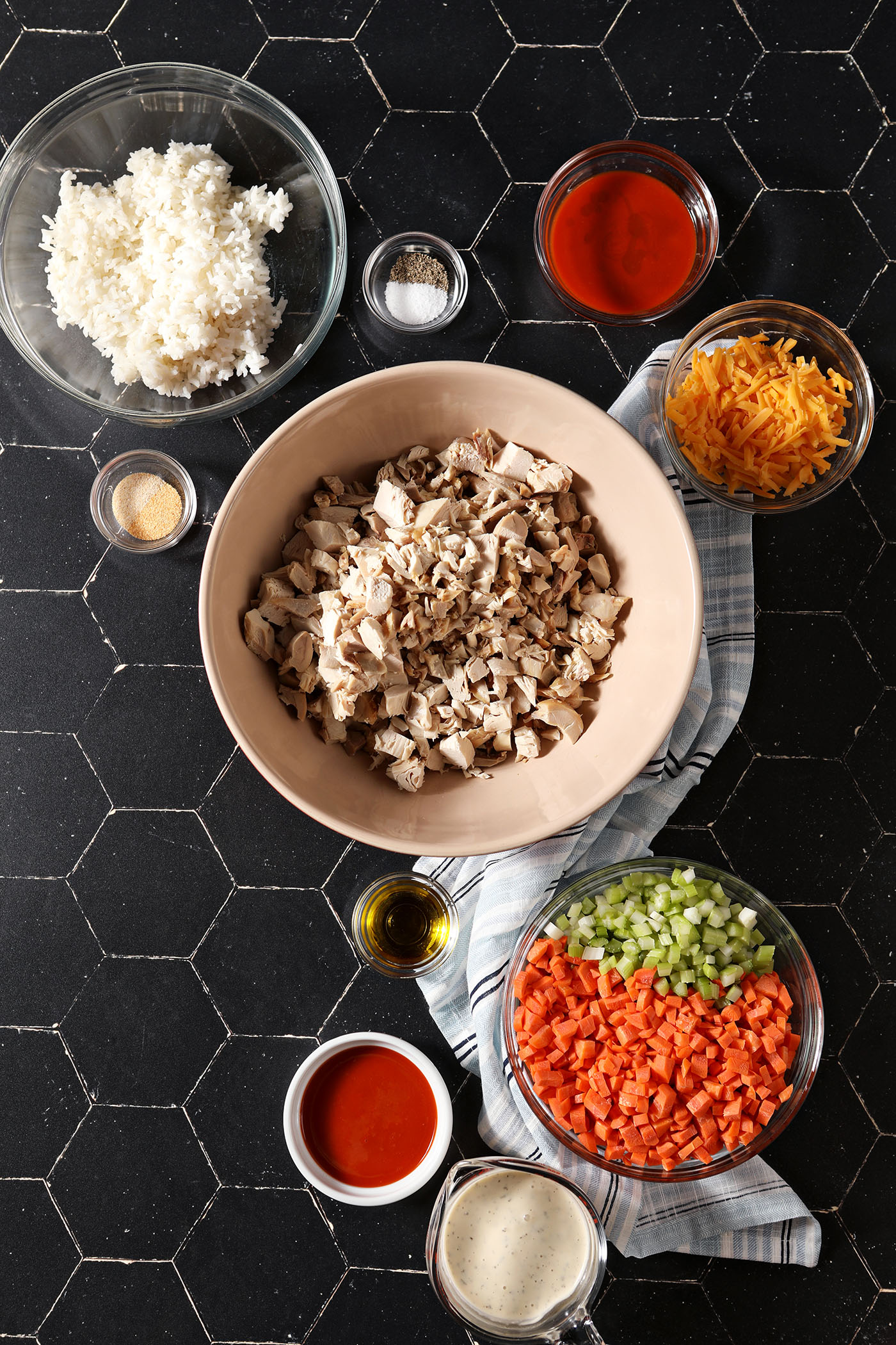 Ingredients to make a buffalo chicken wing casserole in bowls on black tiles