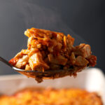 A spoon holds a scoop of buffalo chicken casserole above a casserole dish