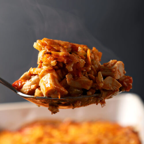 A spoon holds a scoop of buffalo chicken casserole above a casserole dish