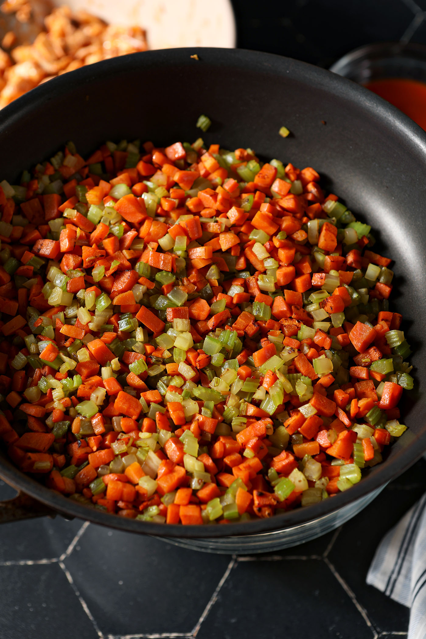 A skillet of sautéed carrots and celery above a black tiled surface