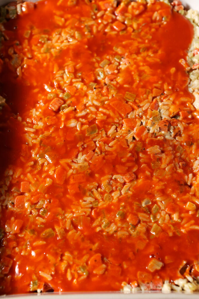 Buffalo sauce on top of a rice mixture in a casserole dish
