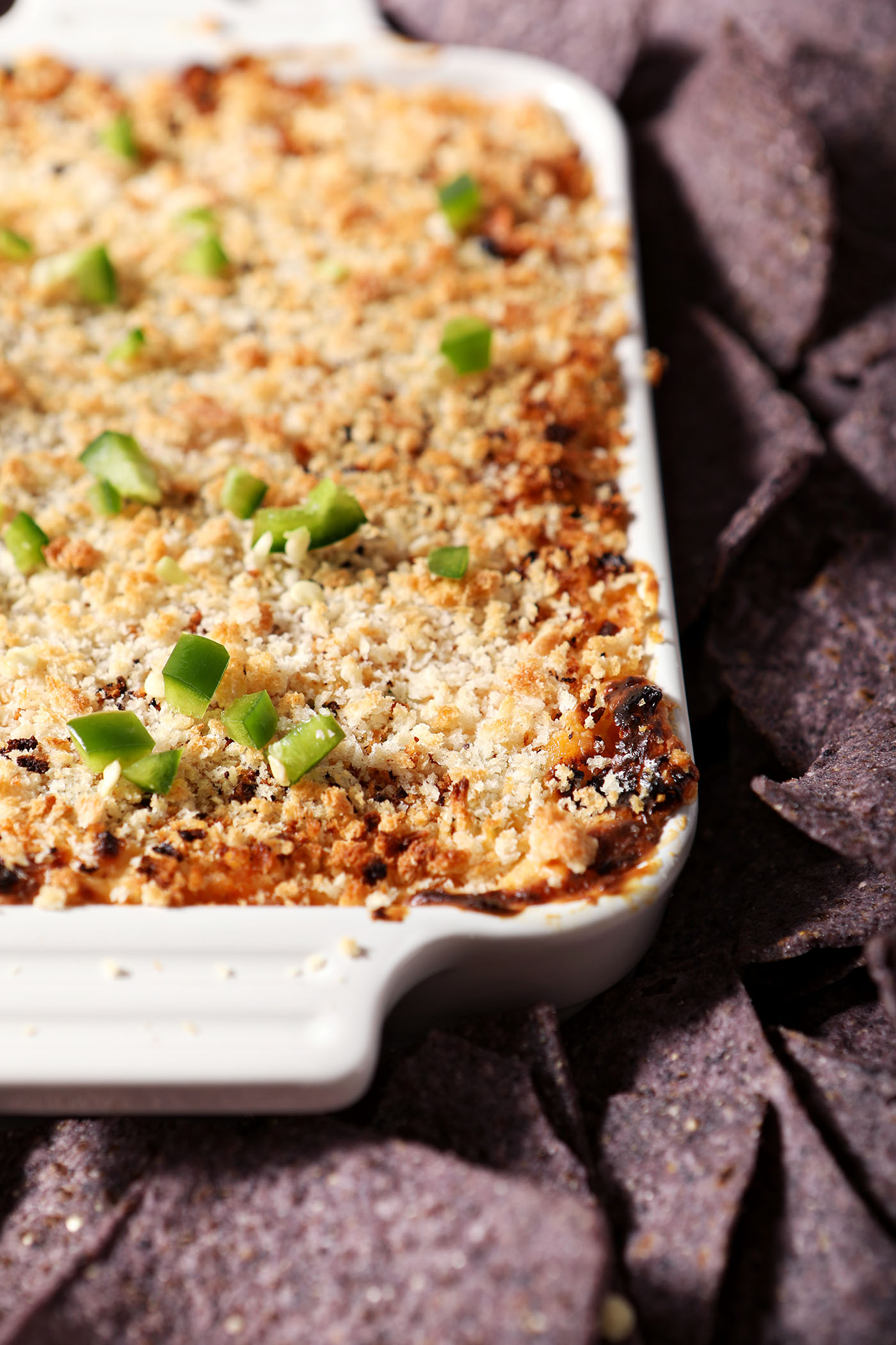 Closeup of a white dish holding baked jalapeno popper dip surrounded by tortilla chips