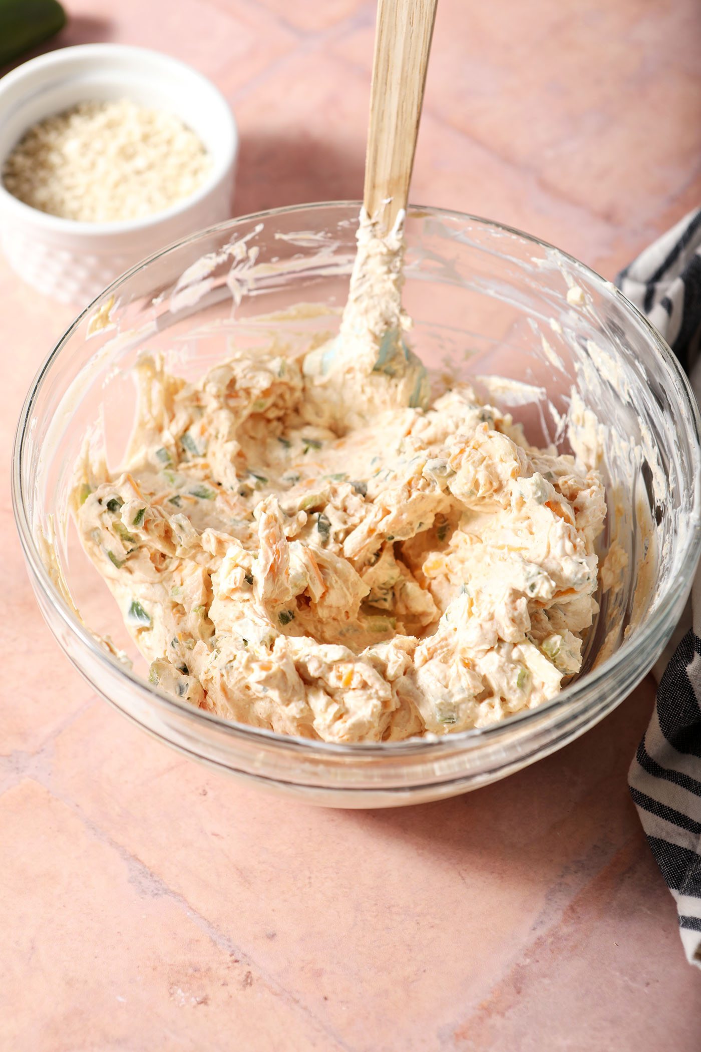 Mixed jalapeño popper dip in a bowl with a small spatula on a terracotta surface
