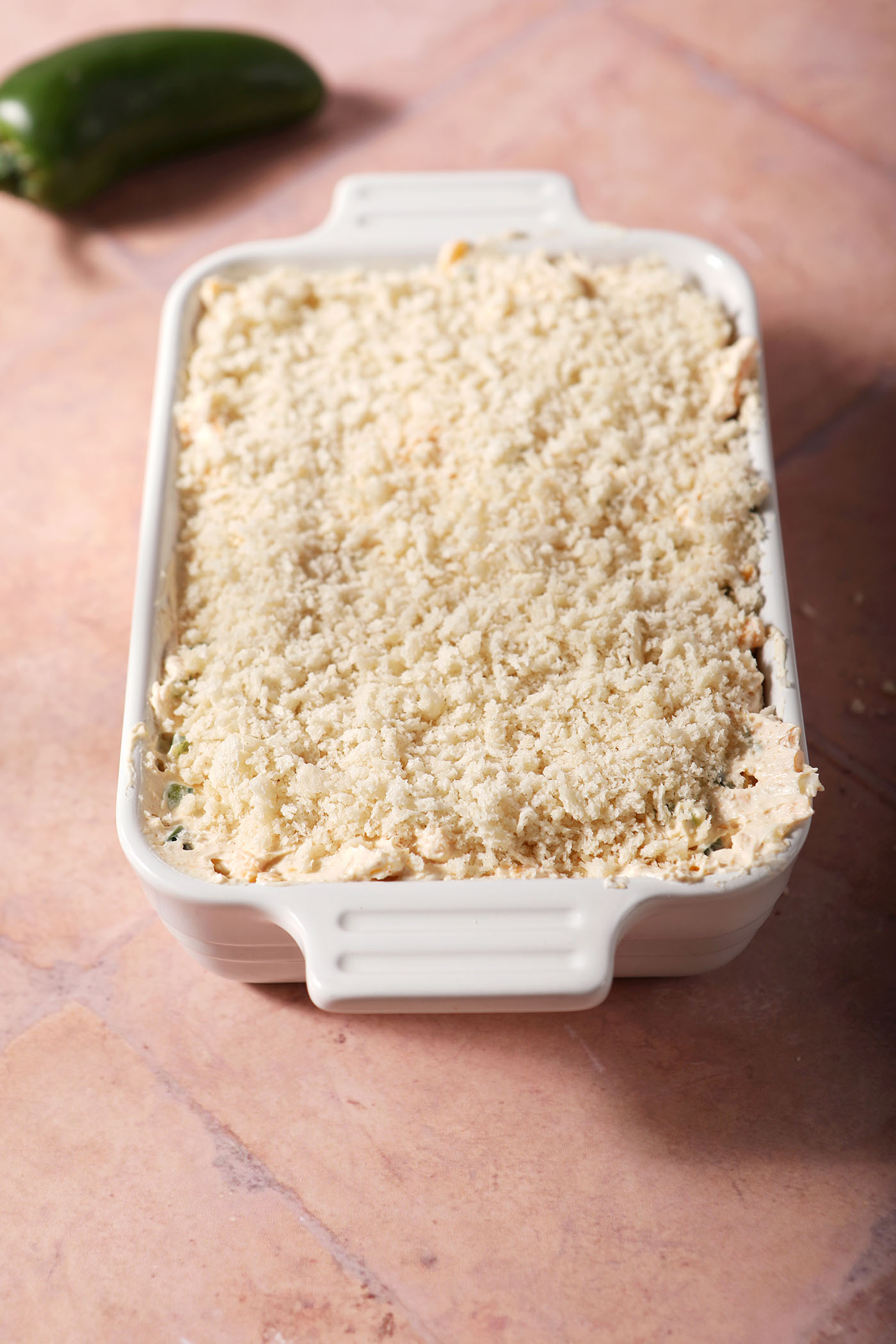 Jalapeno popper dip topped with panko breadcrumbs in a white casserole dish on terracotta, before baking