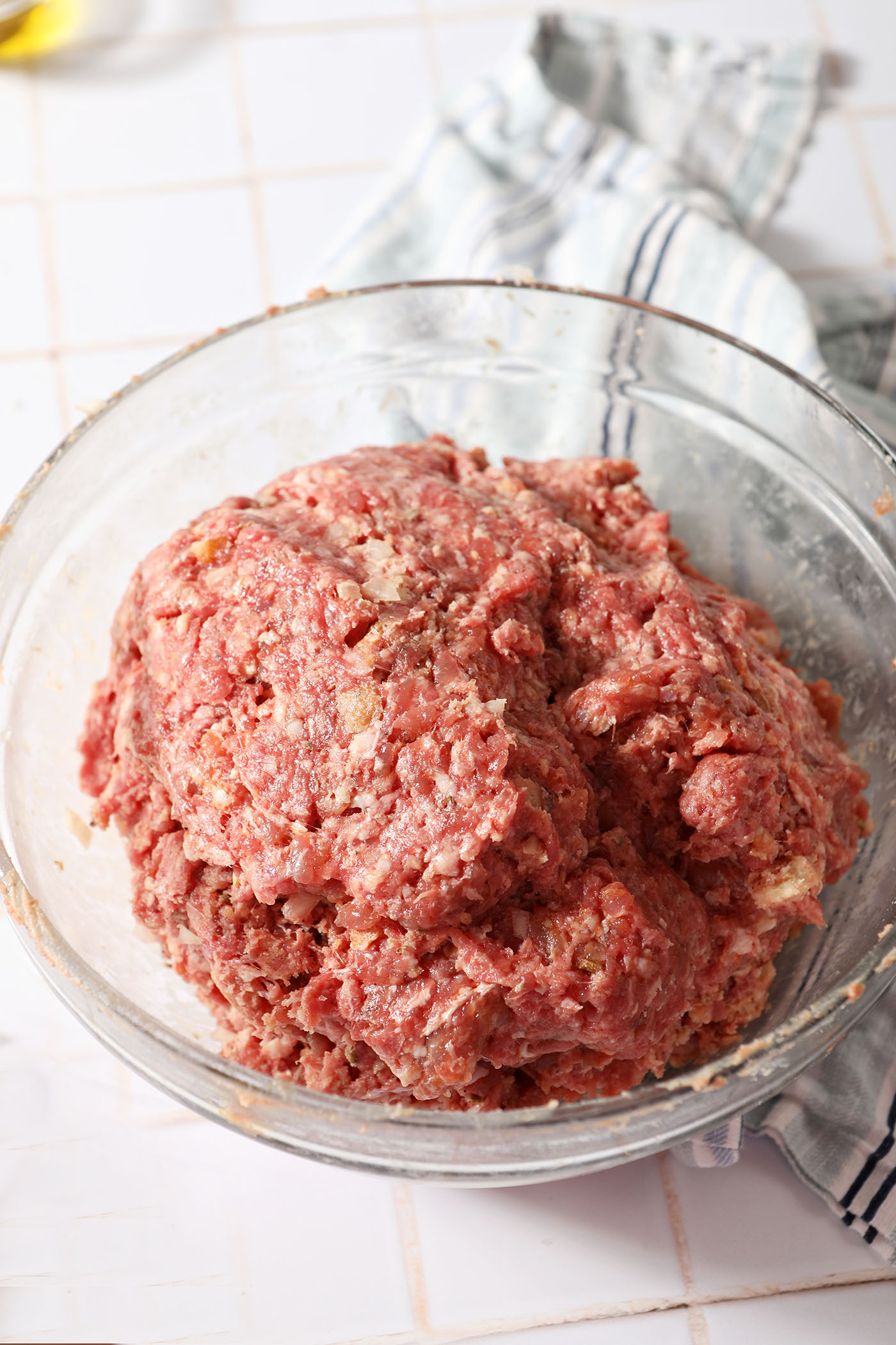 Meatball mixture in a bowl on a white tiled surface before scooping