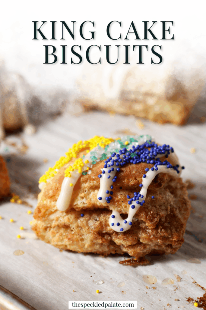 A cinnamon sugar biscuit decorated like a king cake for Mardi Gras sits on a sheet pan near other biscuits with the text king cake biscuits