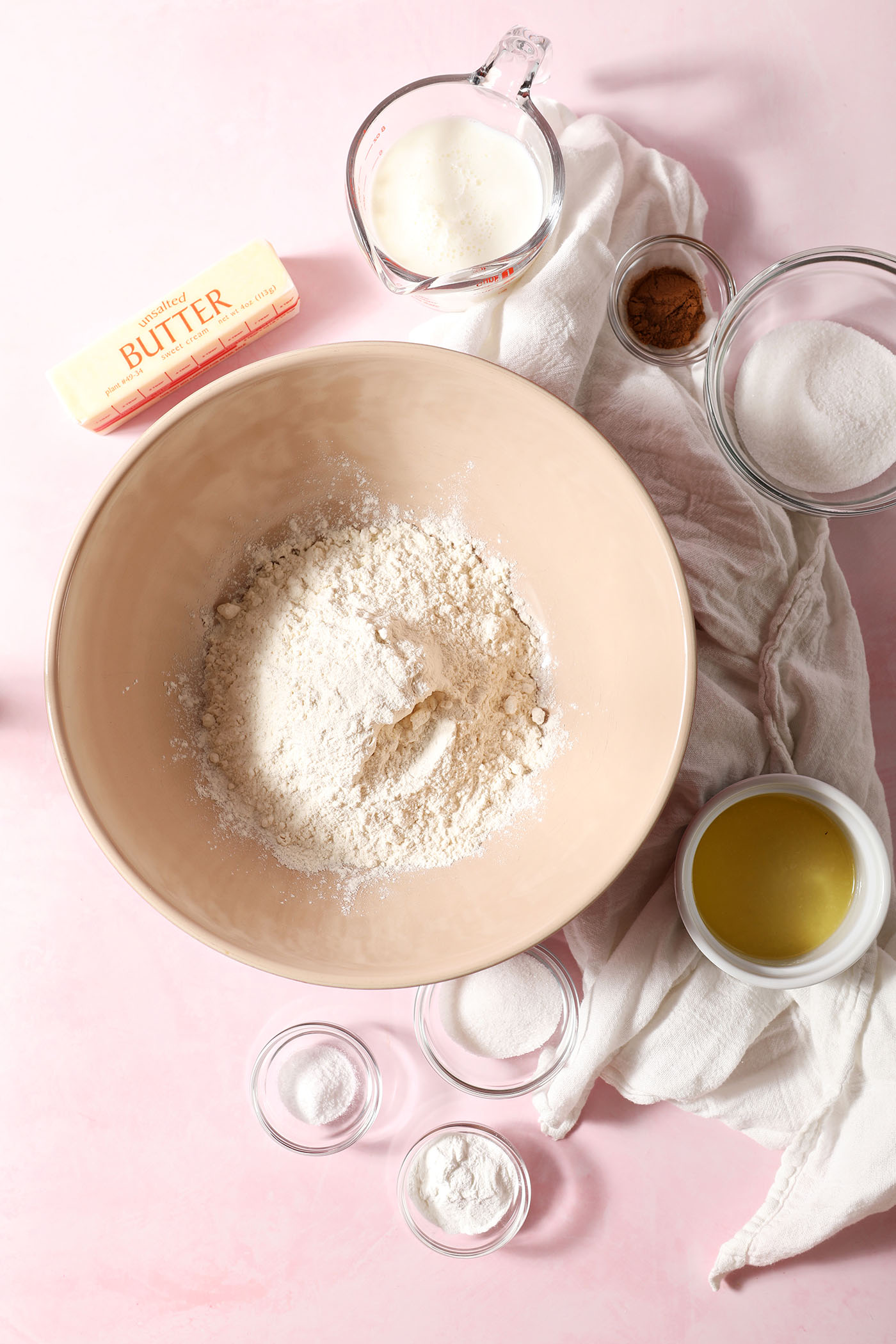Ingredients to make homemade biscuits with a cinnamon sugar swirl in bowls on a pink surface