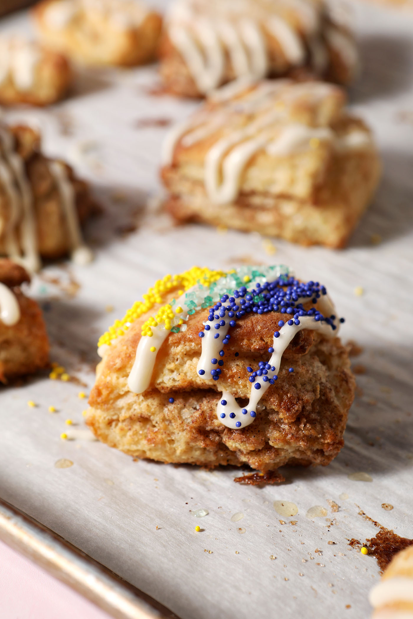 A cinnamon sugar biscuit decorated like a king cake for Mardi Gras sits on a sheet pan near other biscuits