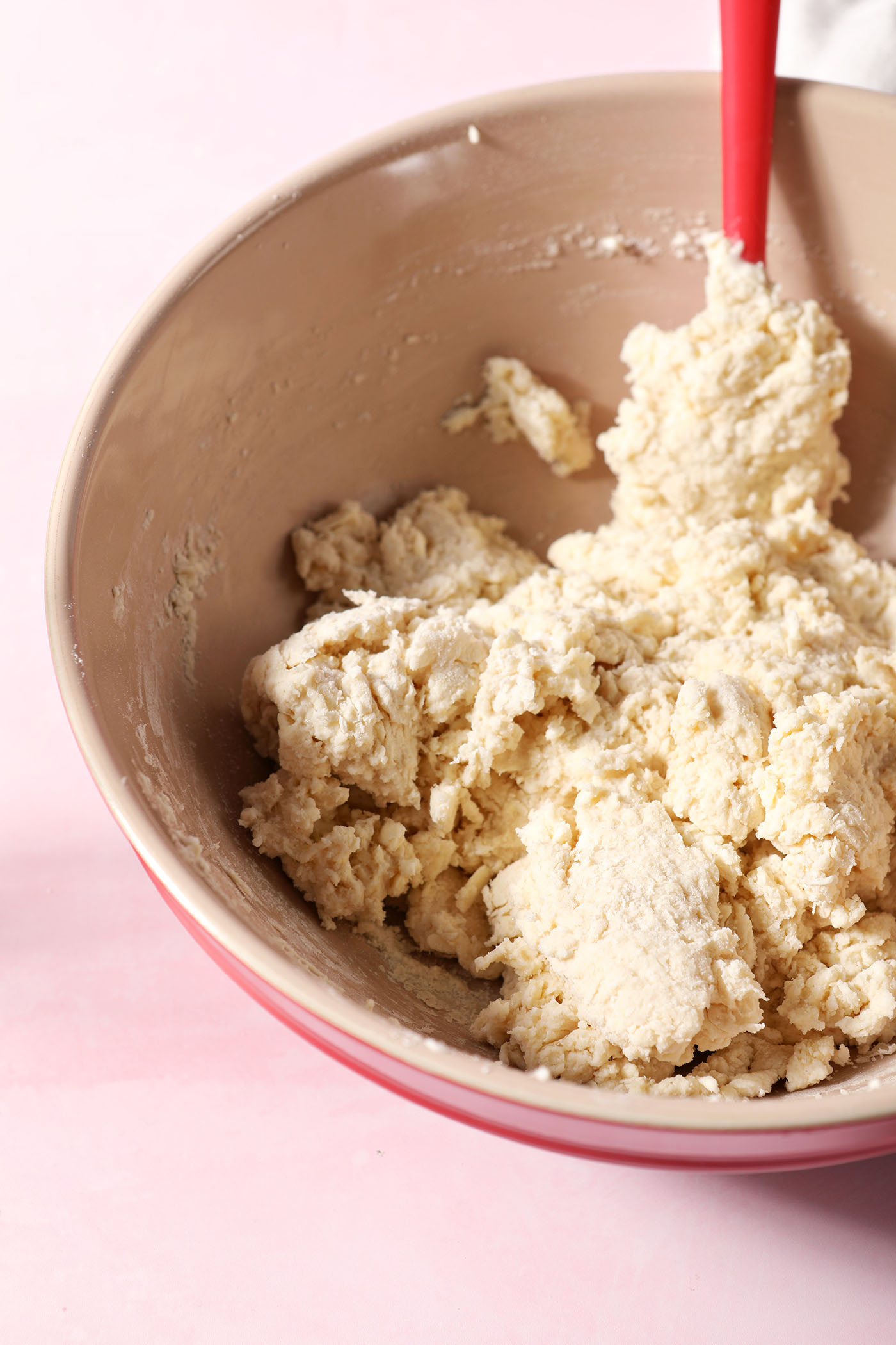 Mixed biscuit dough in a red bowl on a pink surface