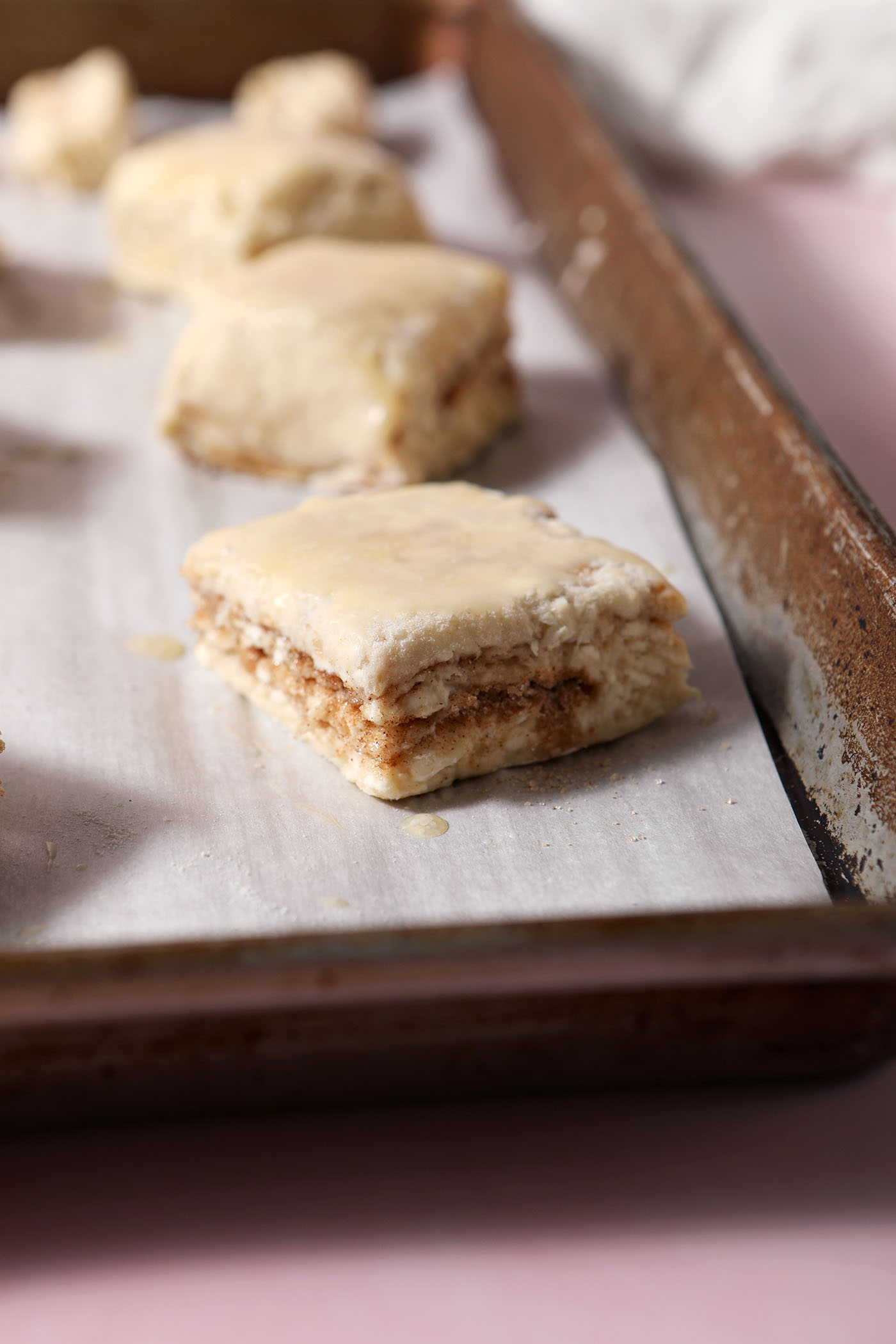 Side angle of butter-brushed biscuits on a parchment lined sheet pan before baking