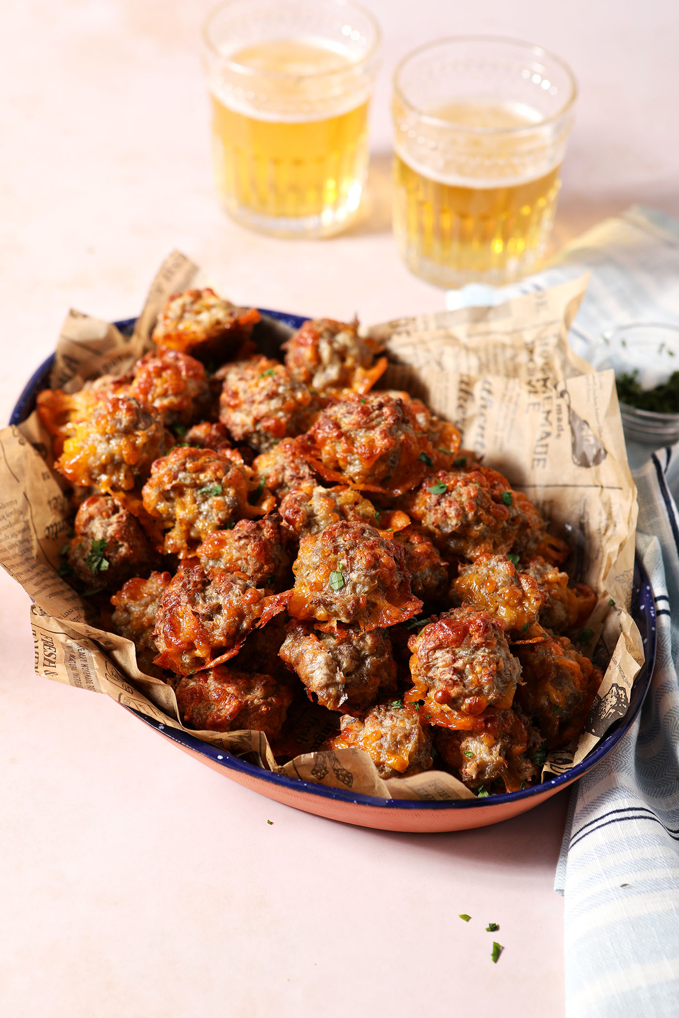 A platter of cream cheese sausage balls without bisquick on a stone surface in front of two glasses of beer