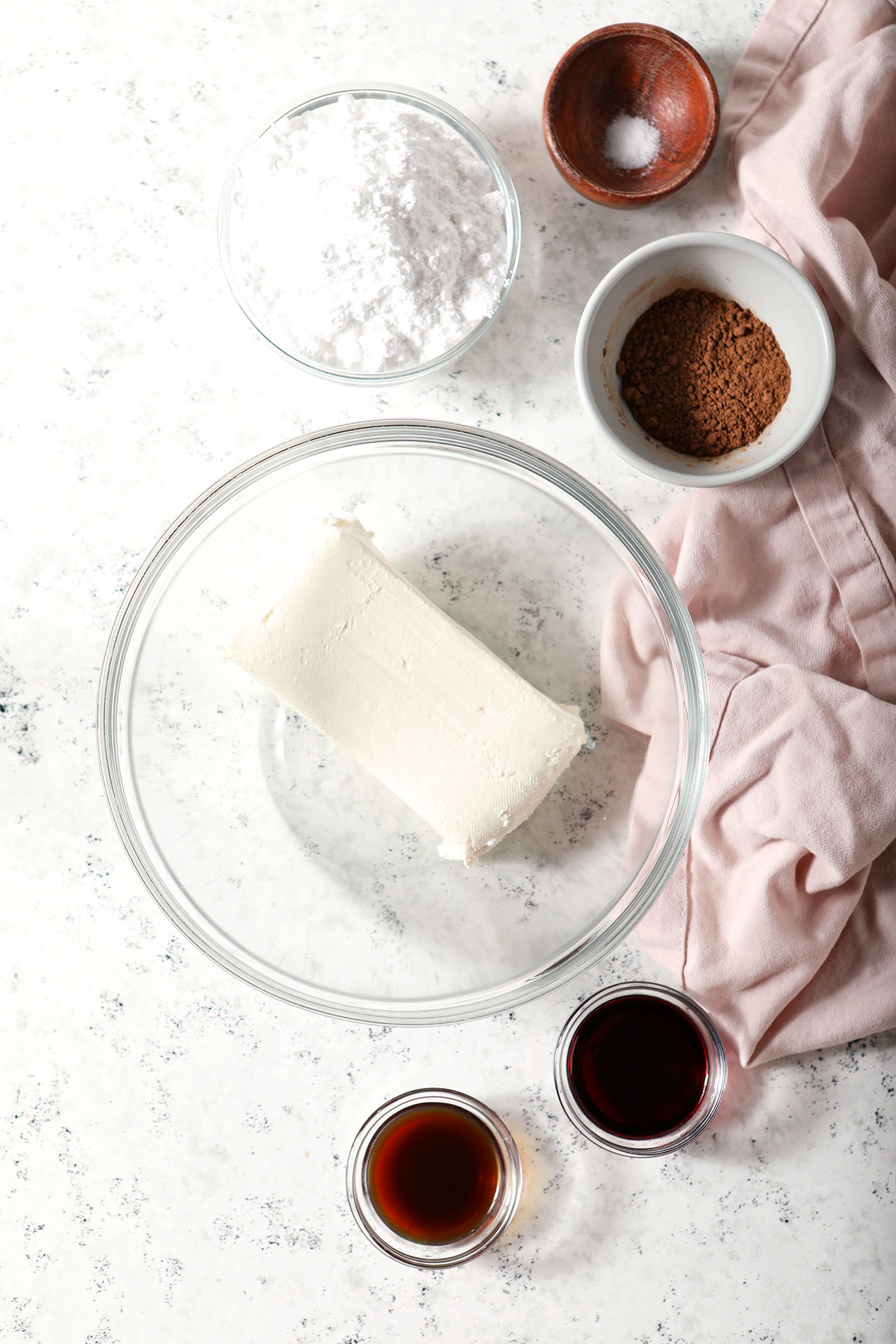 Ingredients to make red velvet dip in bowls on a stoneware surface next to a pink linen