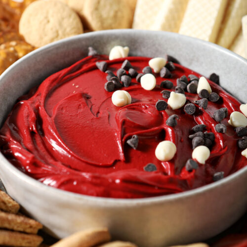 Close up of a bowl holding red velvet dip, garnished with white and regular chocolate chips