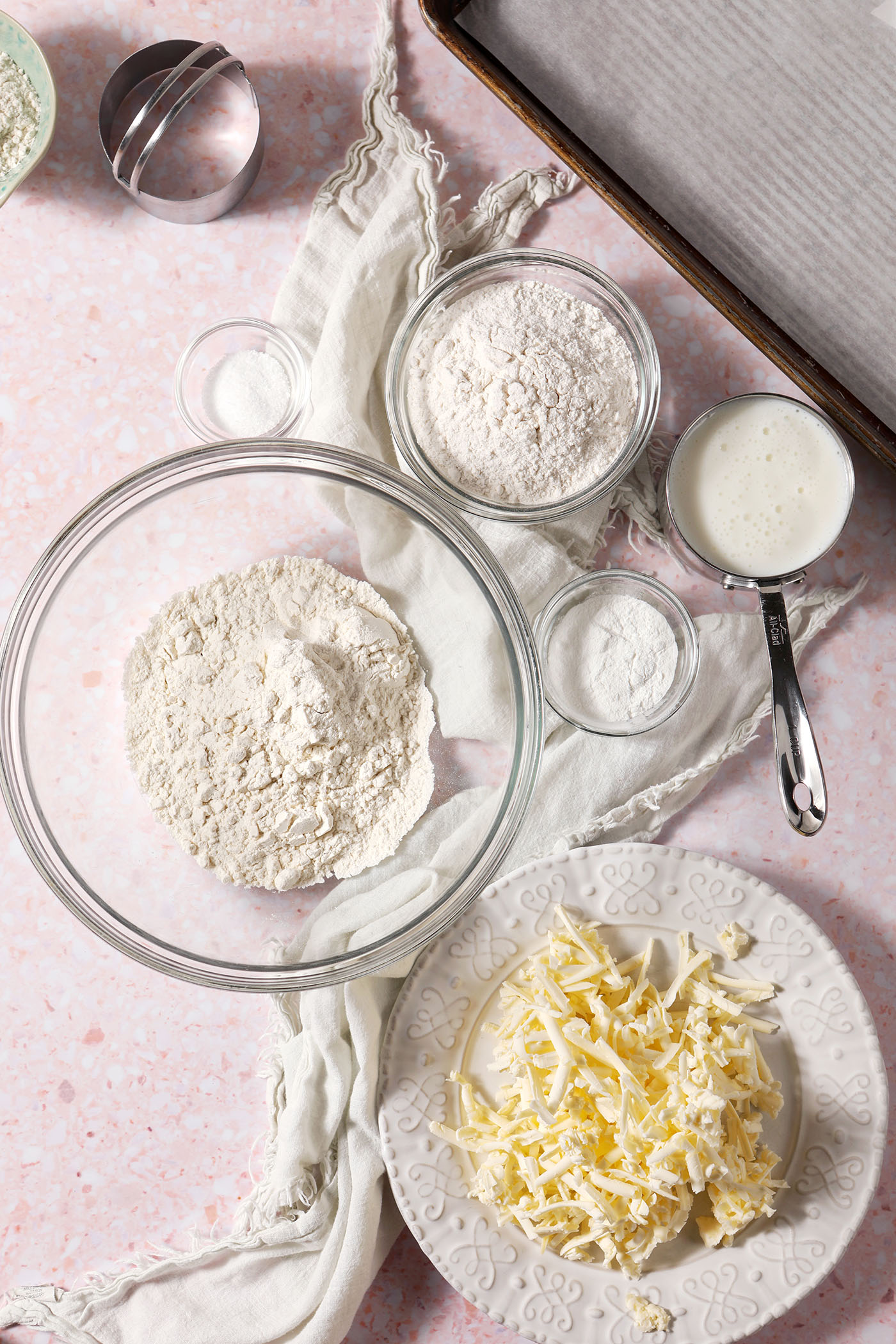 Bowls of ingredients to make buttermilk biscuits on a pink terrazzo surface with a white linen