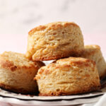 A plate of buttermilk biscuits stacked on a plate on a pink surface