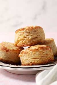 A plate of buttermilk biscuits stacked on a plate on a pink surface