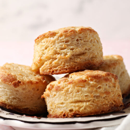 A plate of buttermilk biscuits stacked on a plate on a pink surface