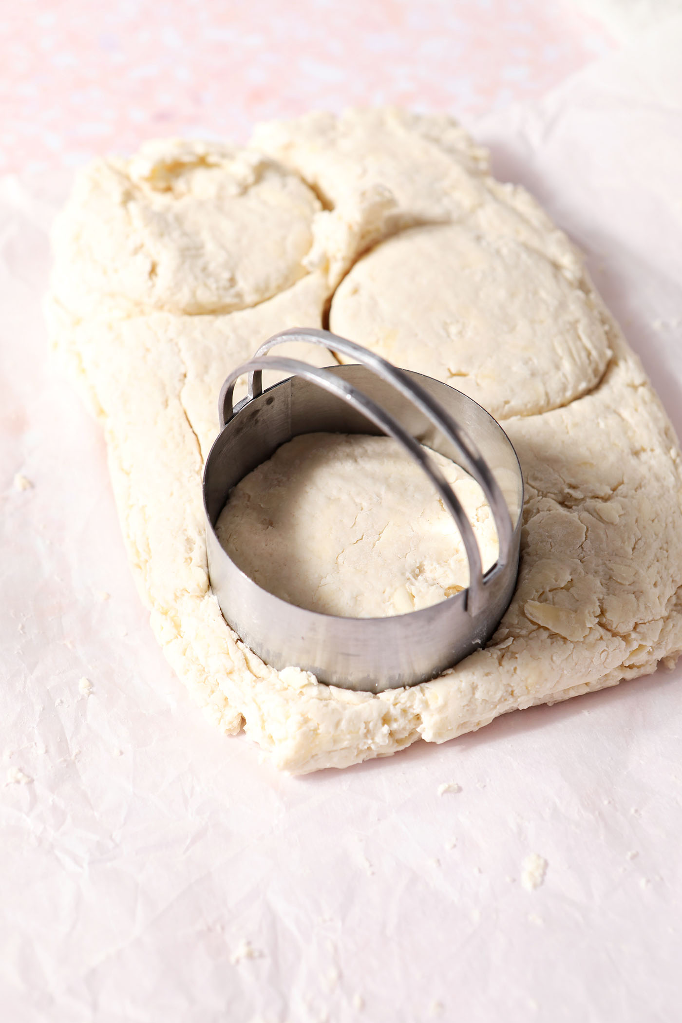 A round biscuit cutter cuts biscuits from a rectangle of biscuit dough
