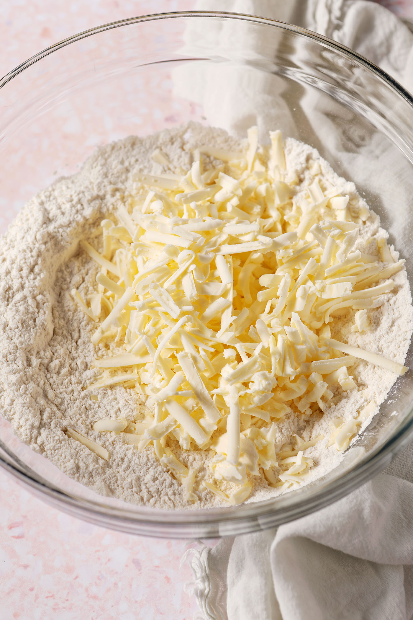 Shredded butter on top of dry ingredients in a bowl on a pink terrazzo surface
