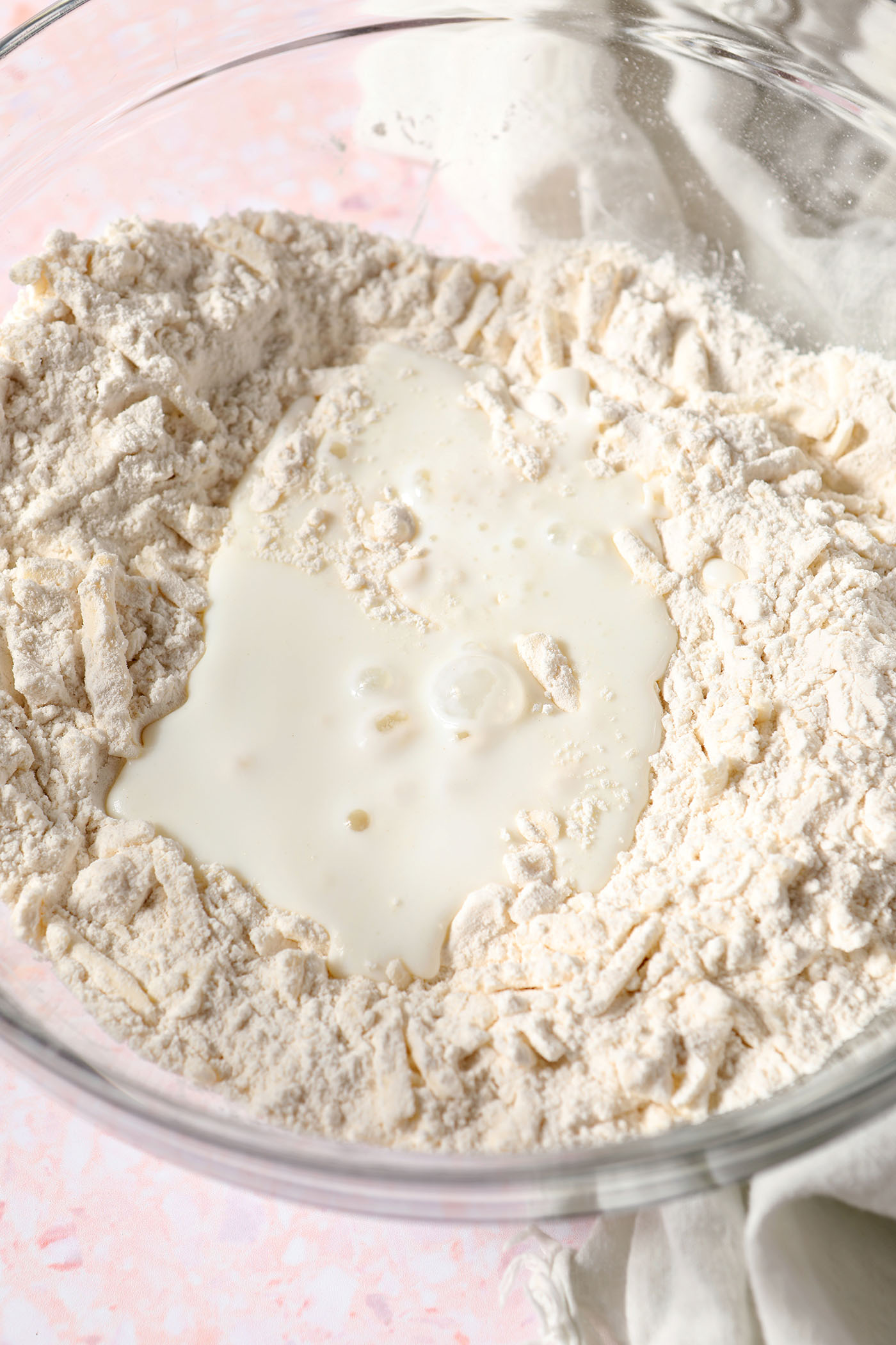 Buttermilk sits on top of dry ingredients for biscuits in a bowl on a pink terrazzo surface