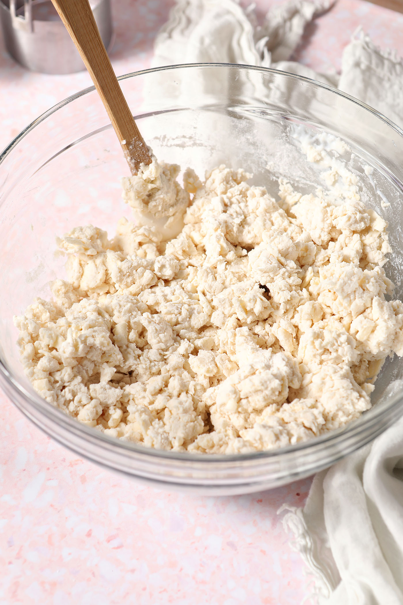 Shaggy biscuit dough in a bowl with a small rubber spatula on a pink terrazzo surface