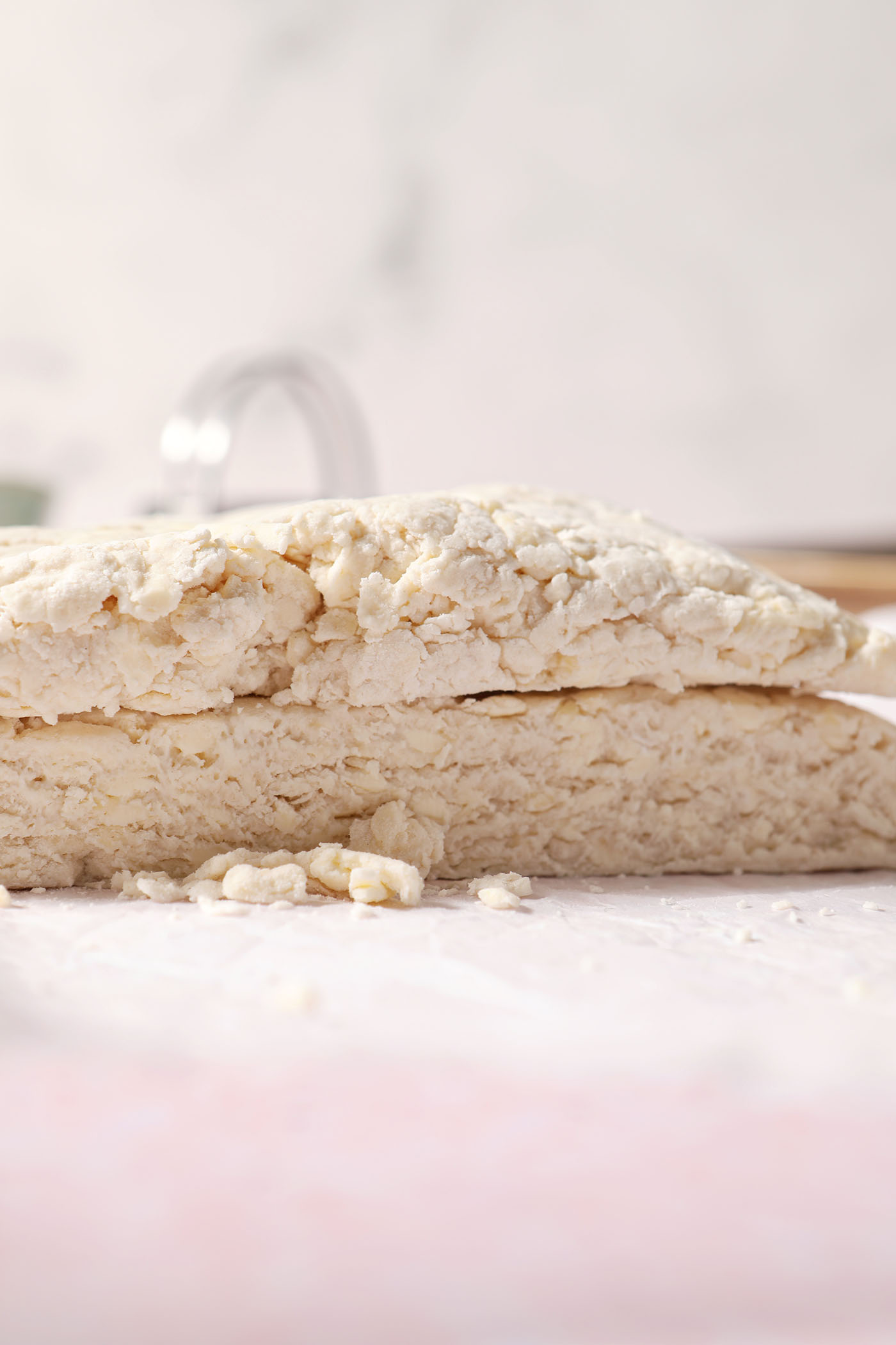 Halved biscuit dough on top of itself during the shaping of biscuits on a sheet of parchment paper