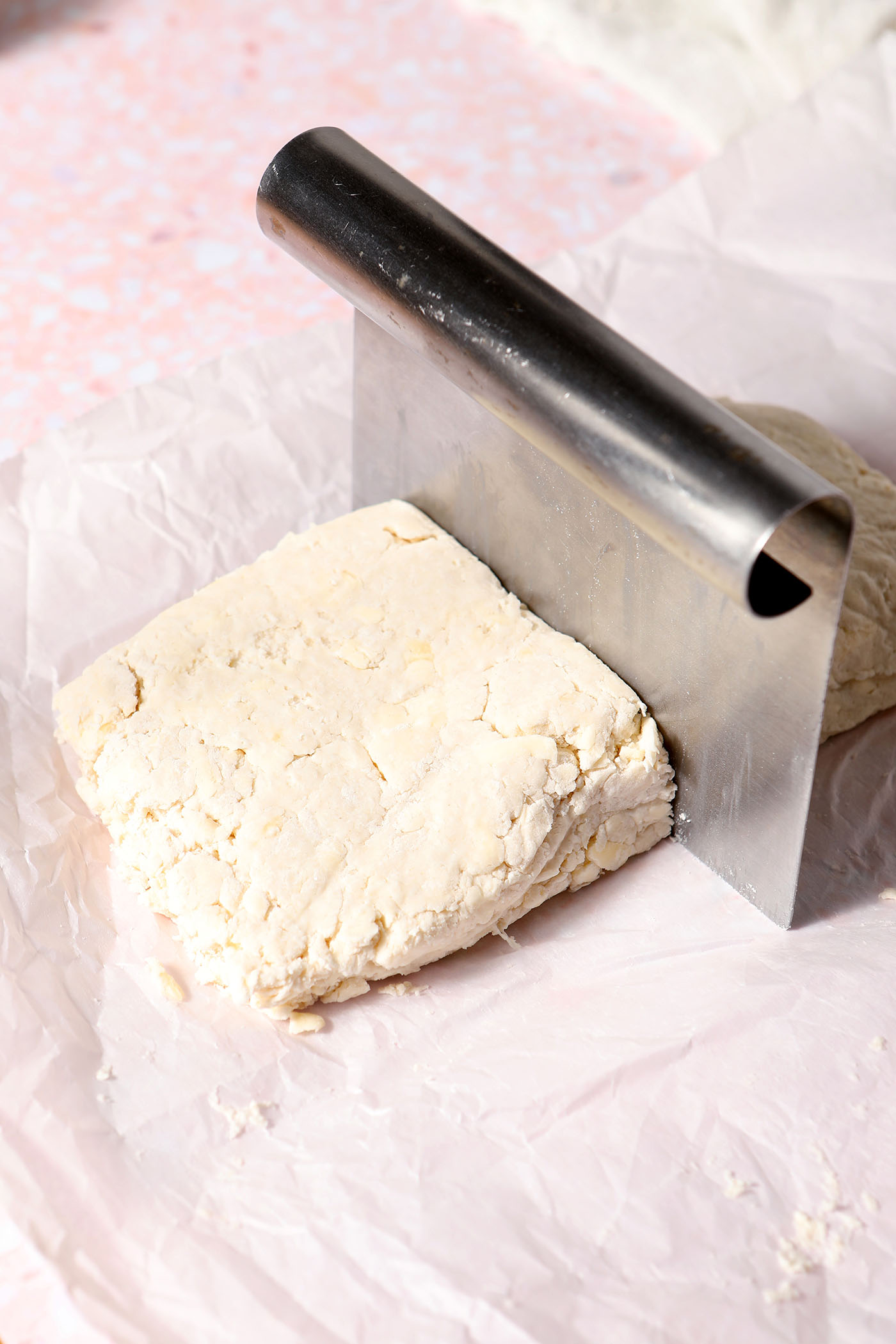 A metal bench scraper halves a rectangle of biscuit dough on a sheet of parchment paper