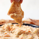 Close up of a hand dipping a chip into carrot cake dip