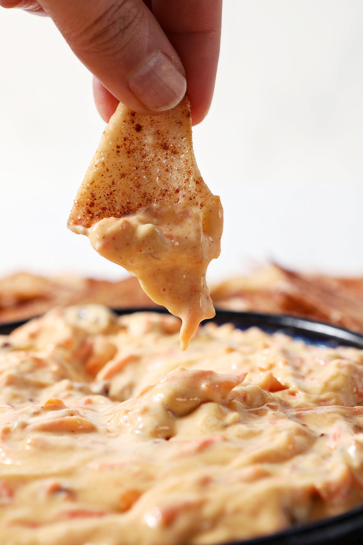 Close up of a hand dipping a chip into carrot cake dip