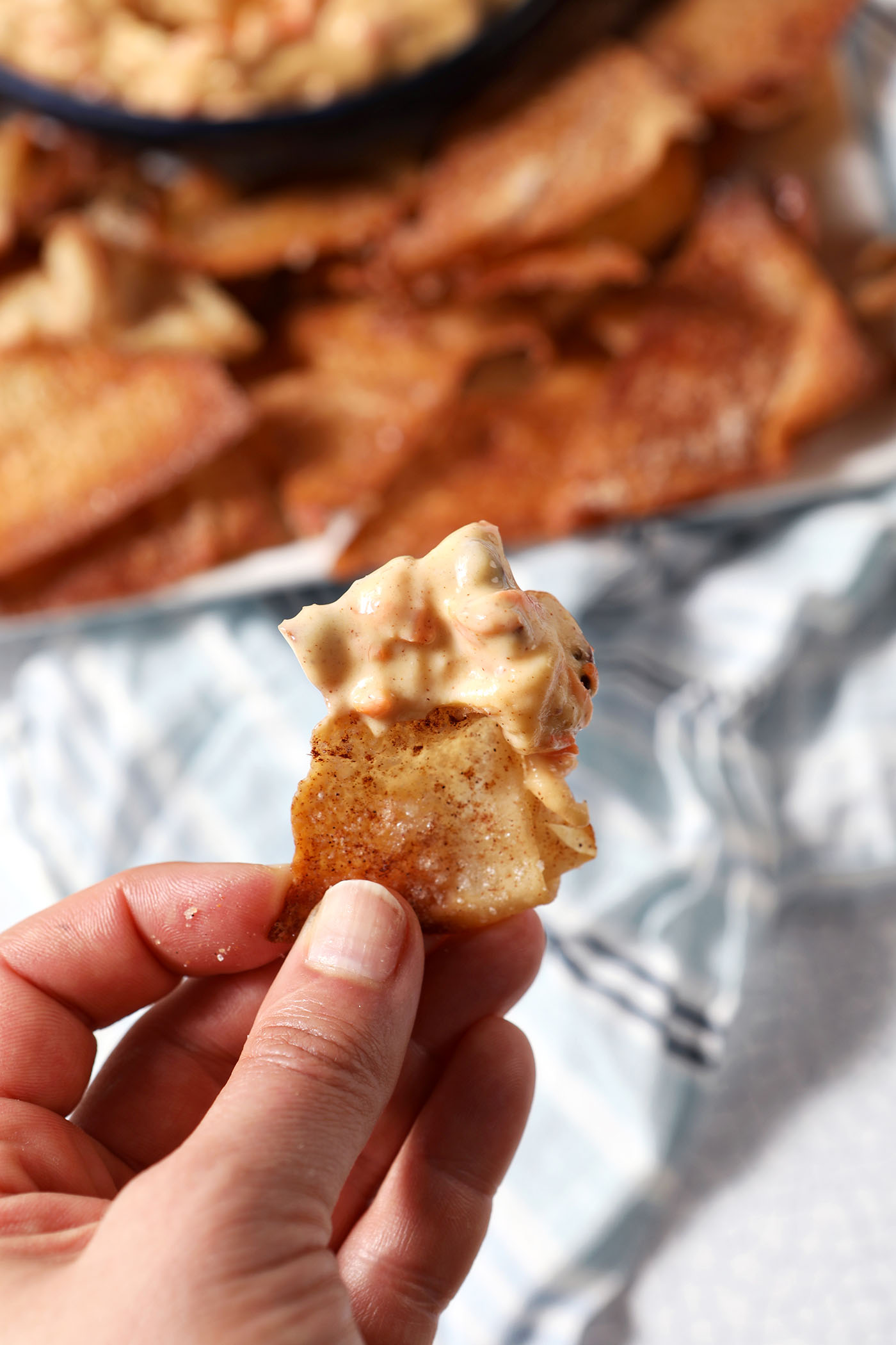 A hand holds a chip covered in carrot cake dip above a blue striped linen