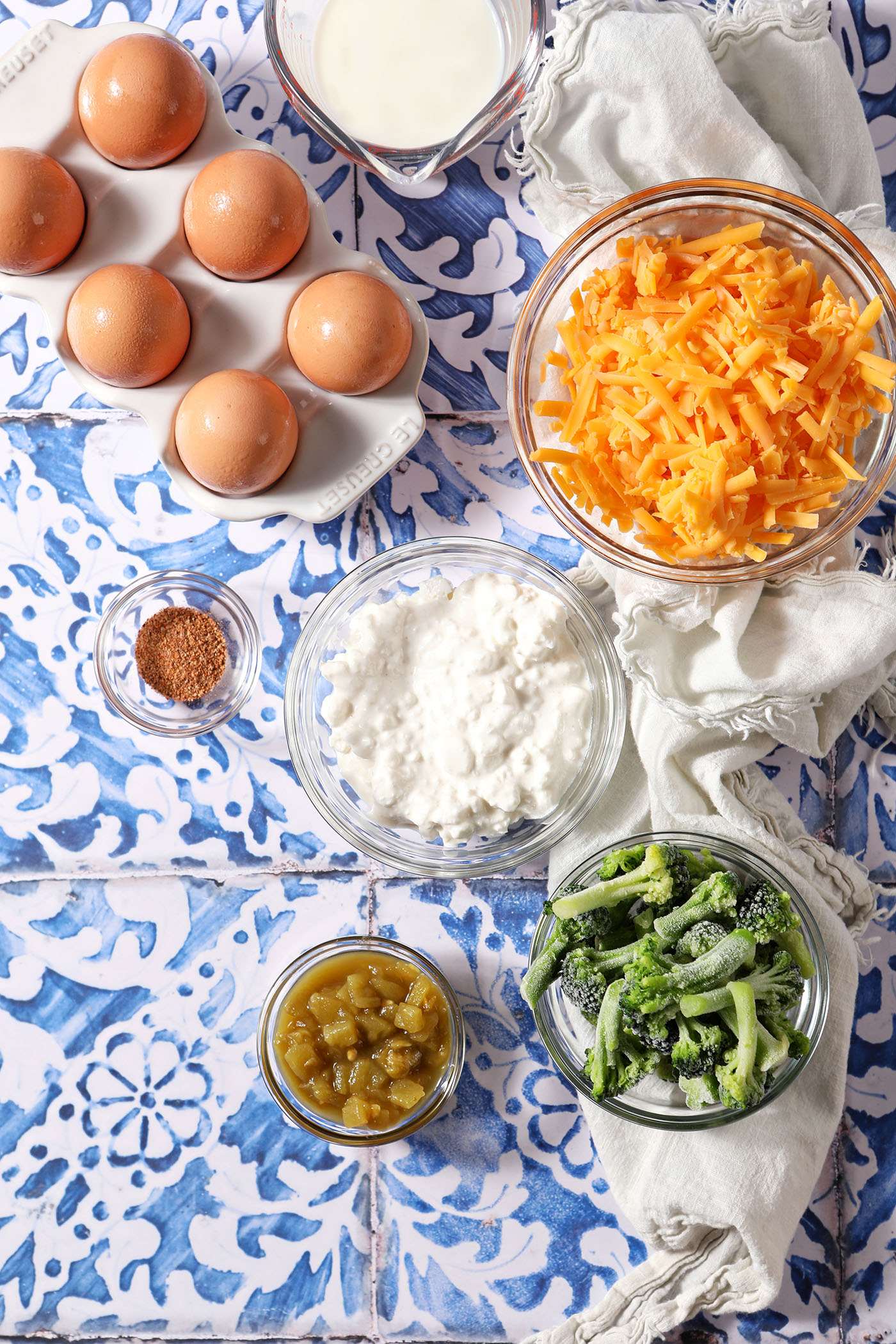 Ingredients to make a cottage cheese quiche without a crust on a blue and white tiled surface