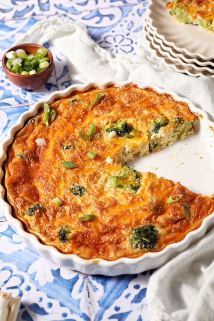 A Crustless Cottage Cheese Quiche with a slice taken out of it on a blue and white tiled surface
