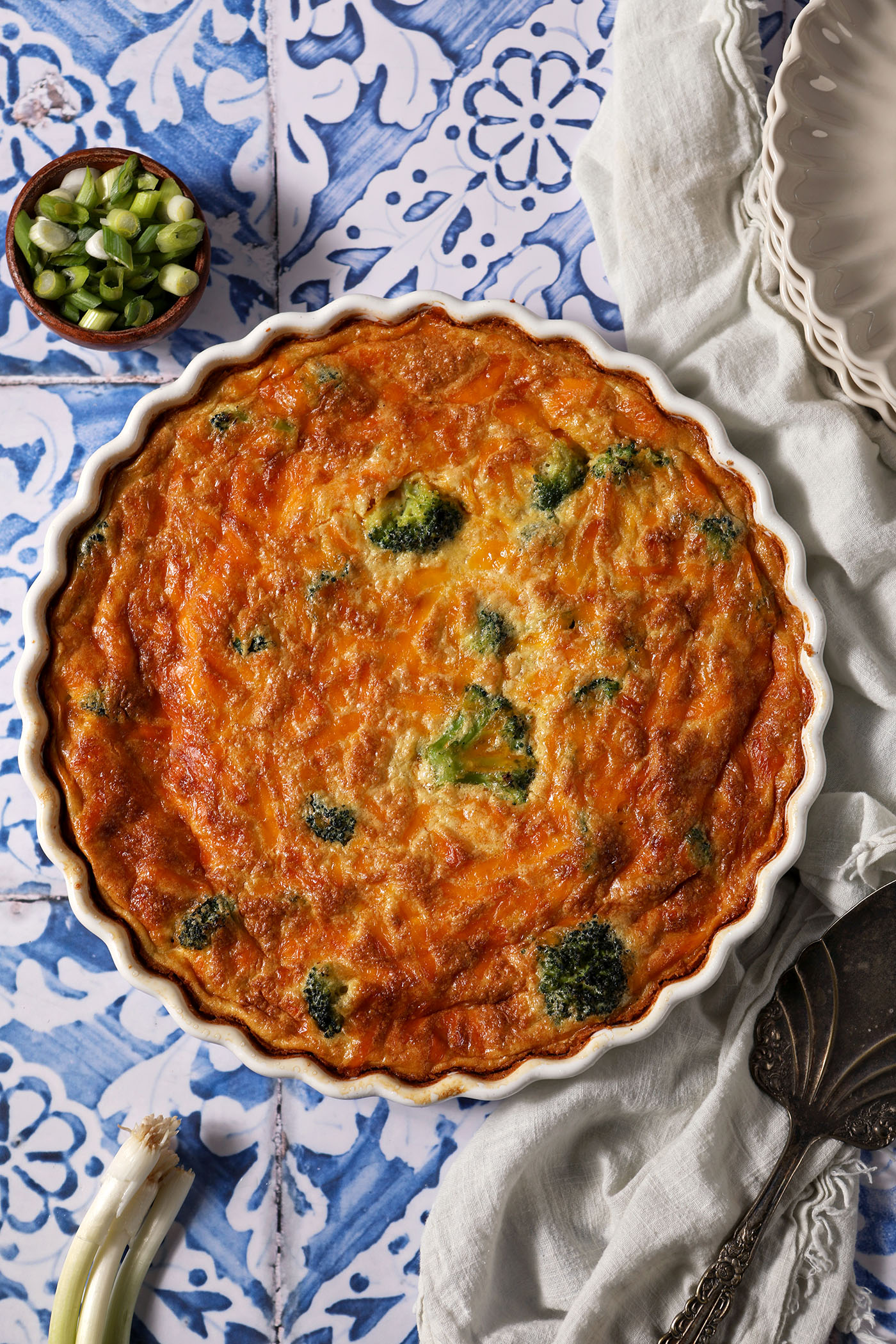 Overhead of a Crustless Cottage Cheese Quiche on a blue and white tiled surface surrounded by green onions
