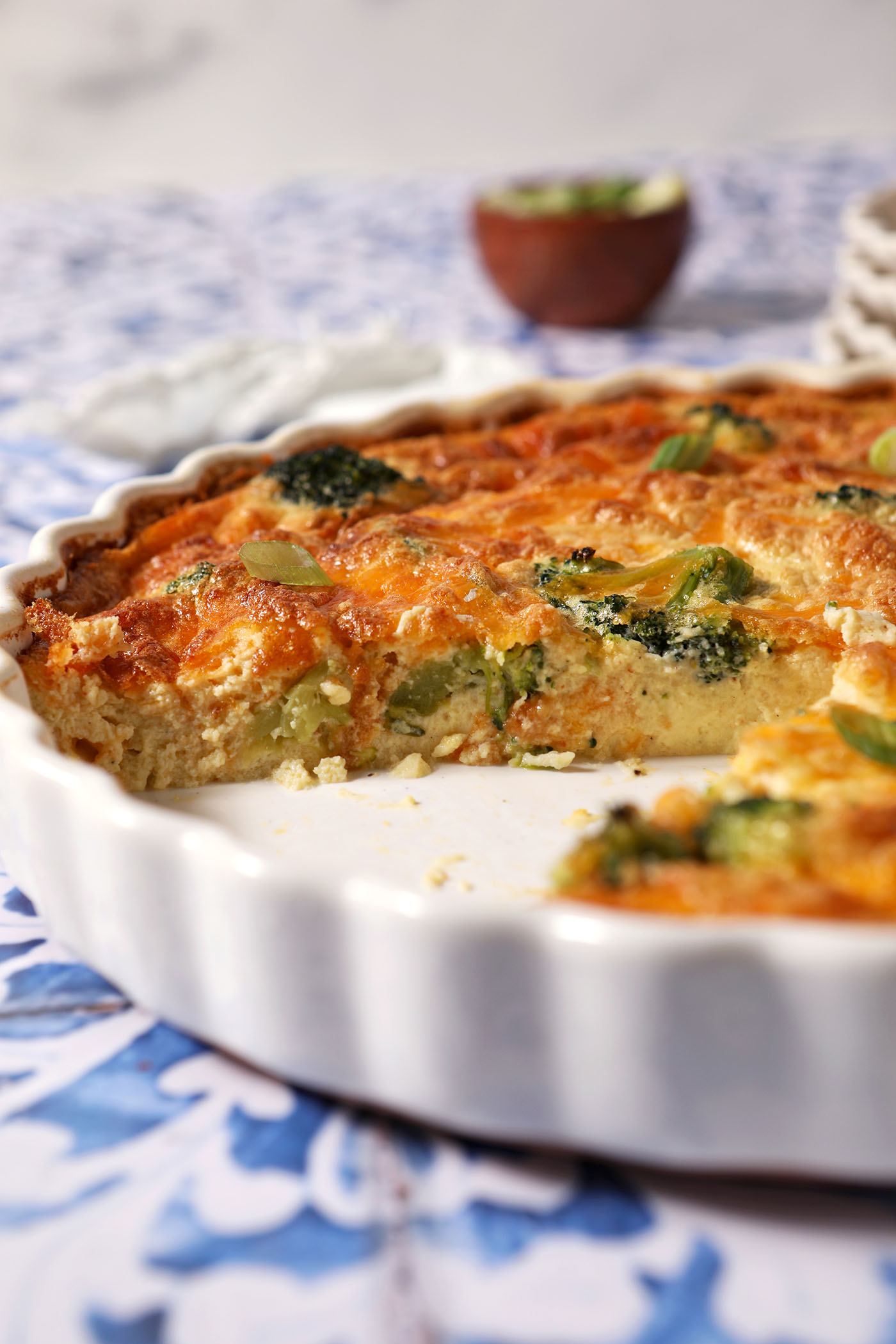 Closeup of the side of a quiche with a slice taken out of it on a blue and white tiled surface