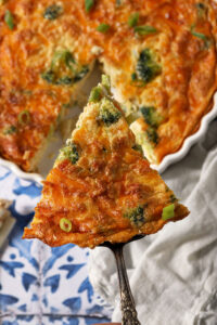A spatula holds a triangular slice of quiche above the rest of a quiche