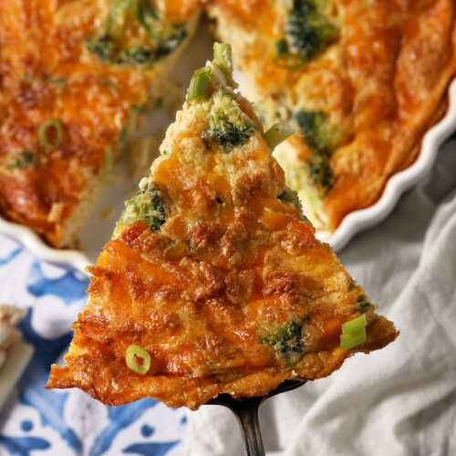 A spatula holds a triangular slice of quiche above the rest of a quiche