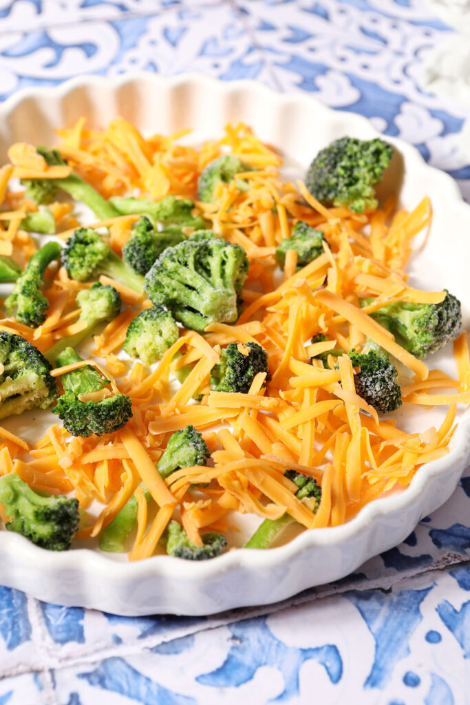 Broccoli and shredded cheddar cheese in a tart pan before quiche liquid is added