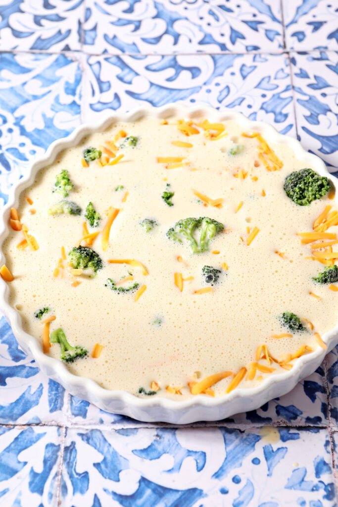 An unbaked quiche in a white tart pan on a blue and white tiled surface