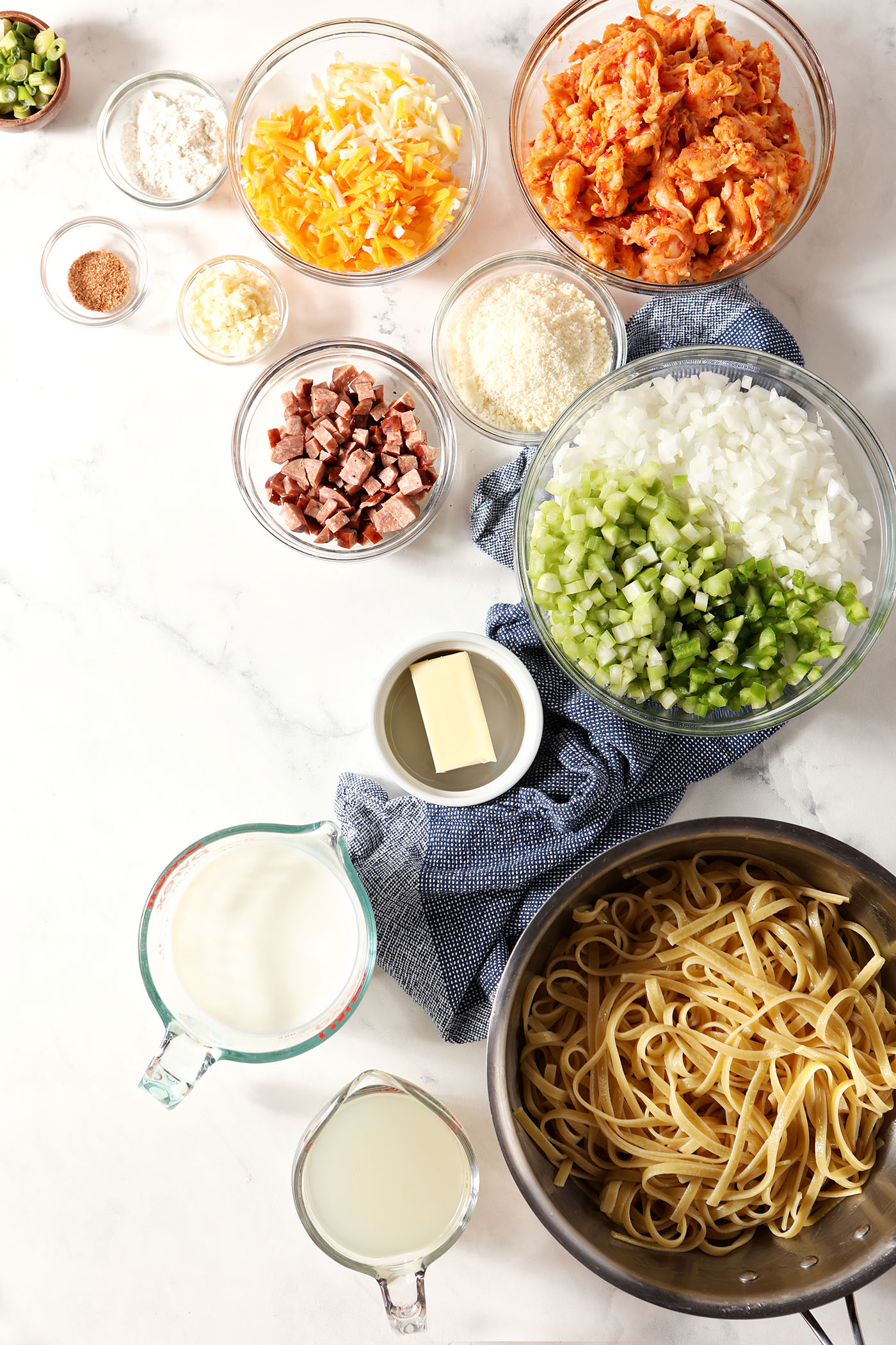 Ingredients to make crawfish pasta in bowls on a marble surface with a blue linen