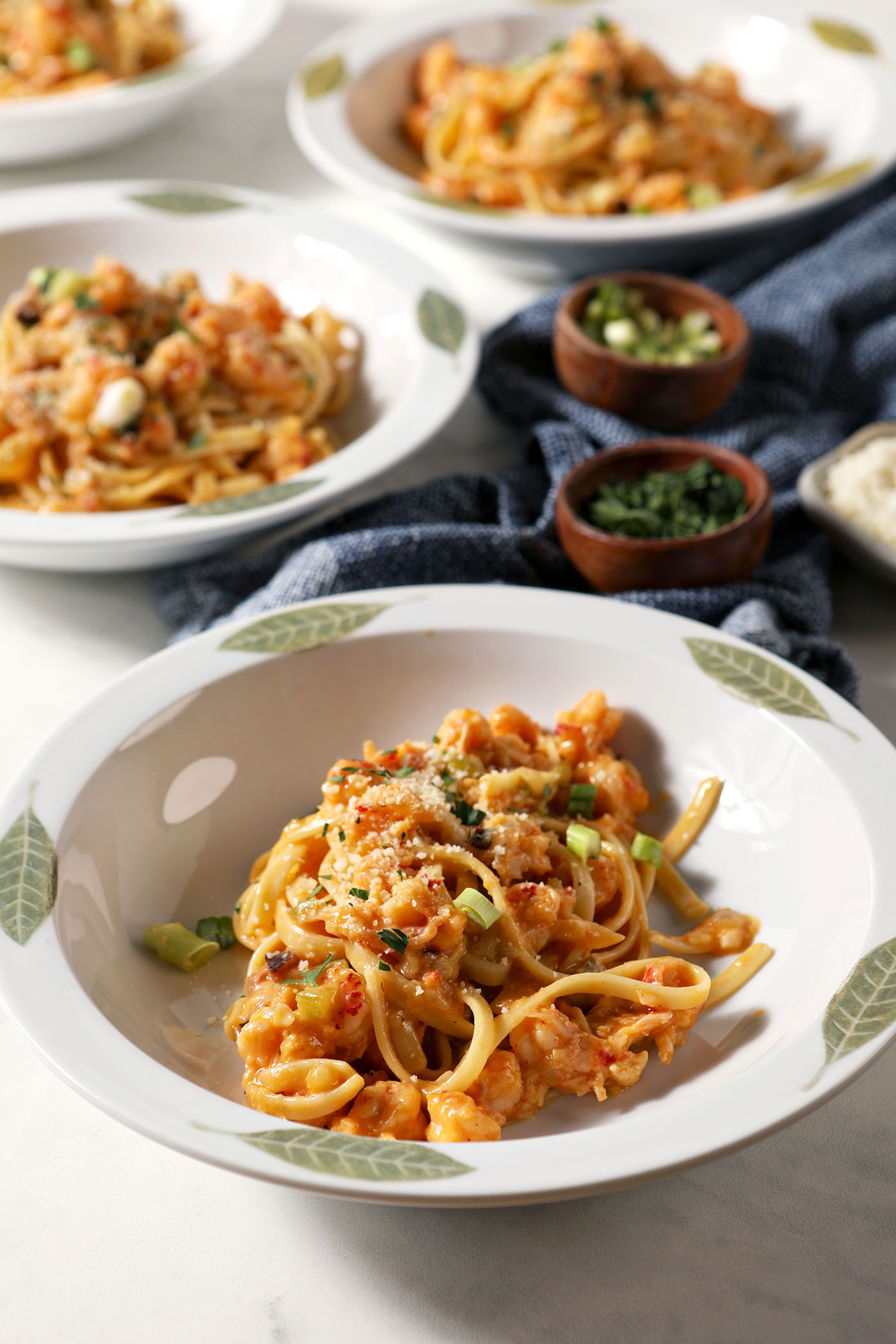 Four bowls of crawfish fettuccine pasta on a marble surface, garnished with parmesan, green onions and parsley, before serving