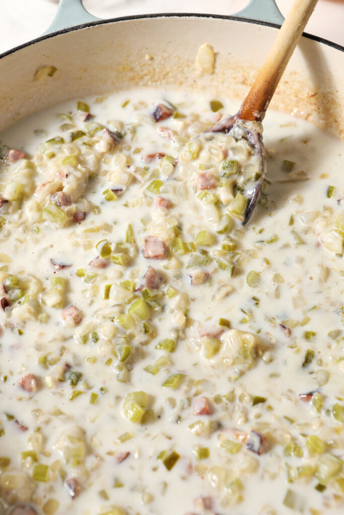 Sautéed vegetables in a milky sauce in a pan with a wooden spoon