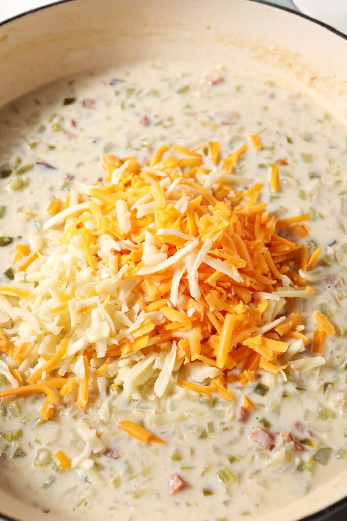 Yellow and orange shredded cheeses on top of a creamy sauce with vegetables